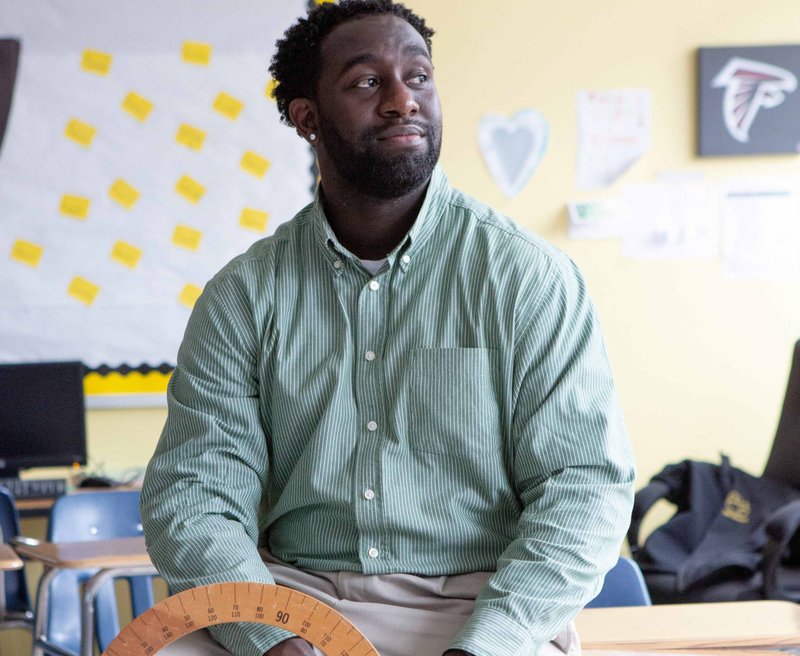 A teacher sits on a desk in a classroom