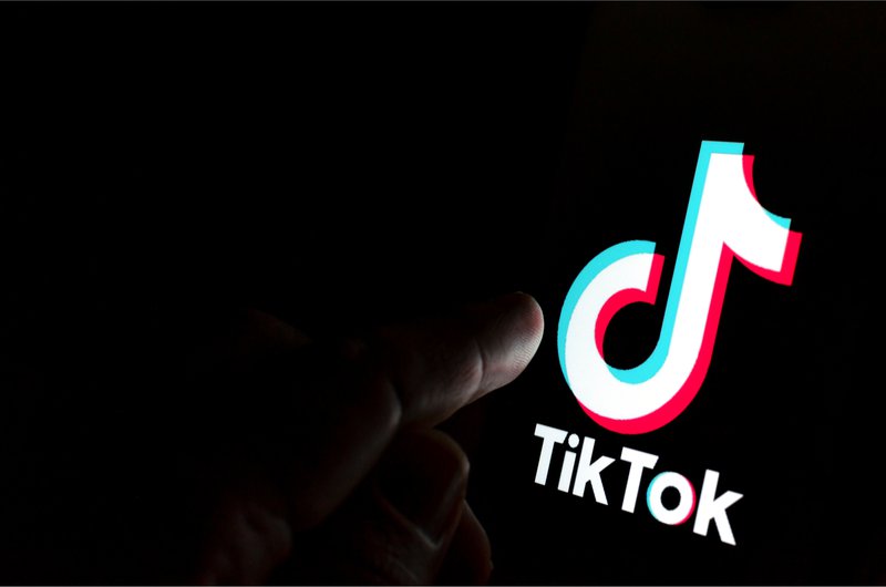 A finger hovers over the TikTok logo that glows in the darkness.